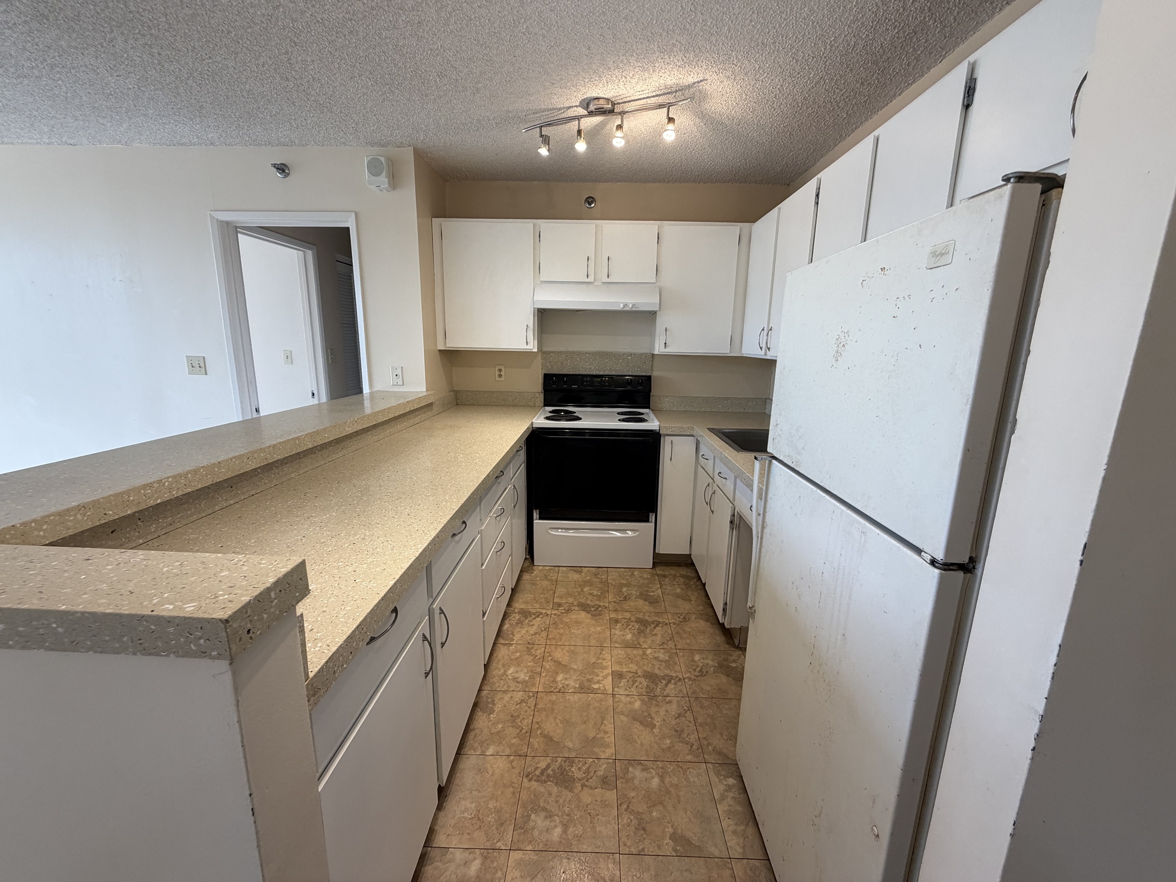 A kitchen with a white fridge, black stove and white cabinets.